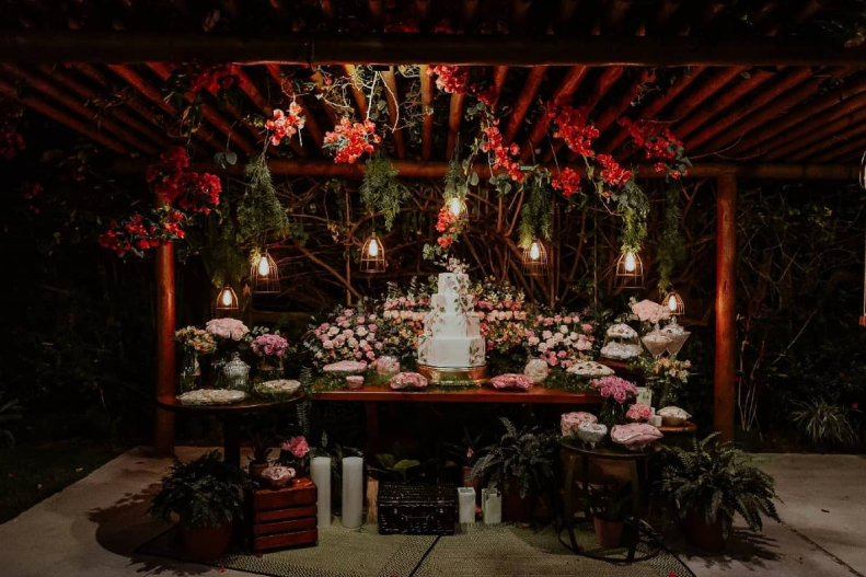 Uma mesa belamente decorada com flores, com diversos doces e o bolo de casamento no centro.